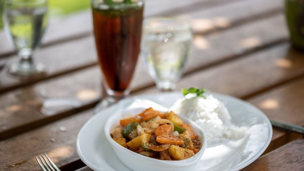 Savory chicken curry served with white rice on a plate by tall iced drink in Tambua Restaurant at Tambua Sands Beach Resort
