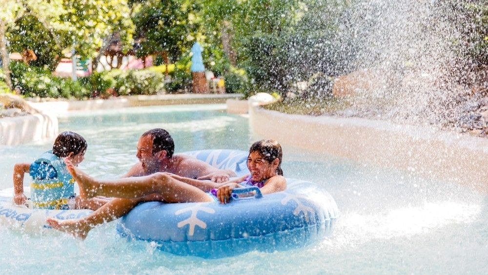 A dad and two childrenin inner tubes floating in a lazy river are blasted by a spray of water at Disney's Blizzard Beach water park in Orlando.