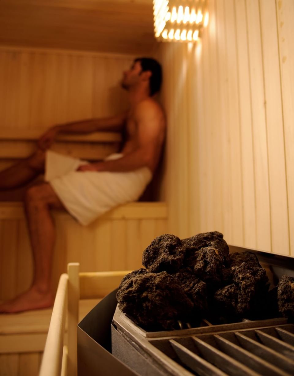 Pedras quentes da sauna junto a parede de madeira sob luz quente perto de hóspede no Noi Spa no NOI Vitacura