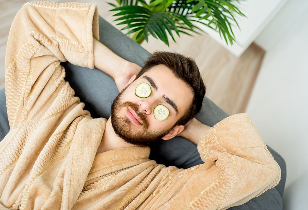 man in yellow bathrobe with cucumber over his eyes