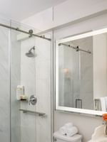 Marble walk-in shower by a large lighted mirror under a soft ceiling glow in Deluxe Double at Warwick Melrose Dallas