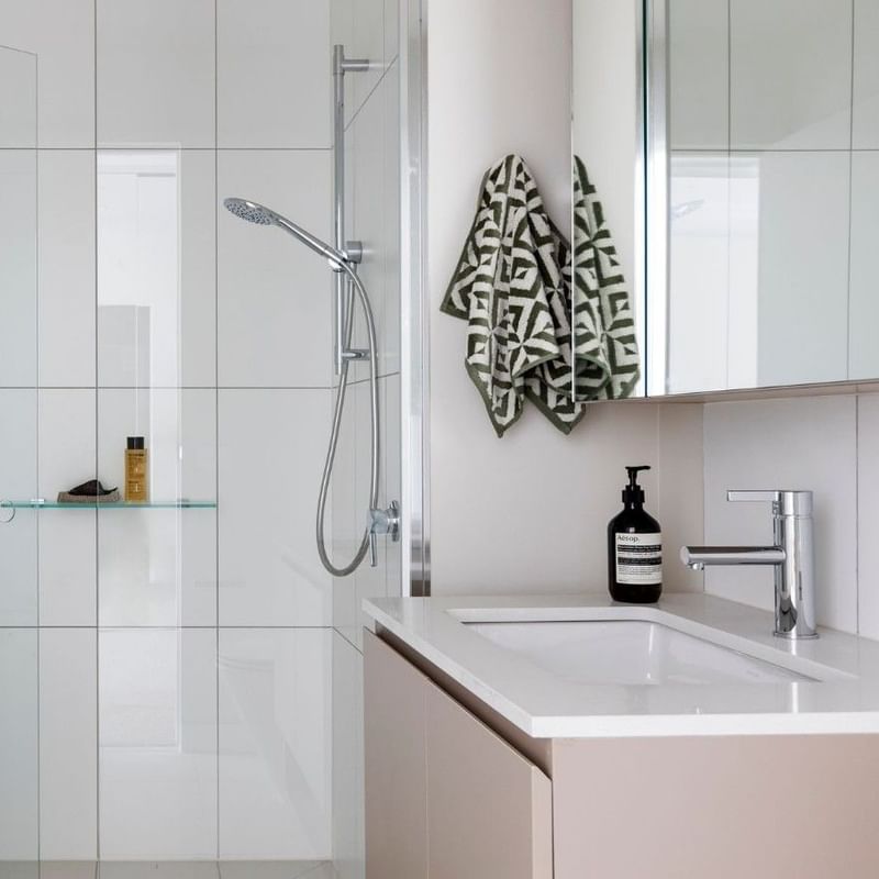 Modern bathroom with white tiles, glass shower, and geometric-patterned towels.