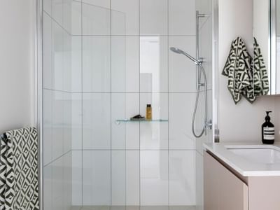 Modern bathroom with white tiles, glass shower, and geometric-patterned towels.