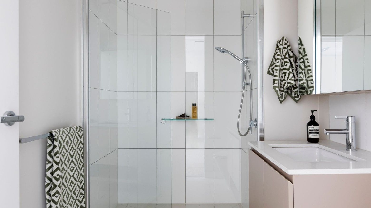 Modern bathroom with white tiles, glass shower, and geometric-patterned towels.