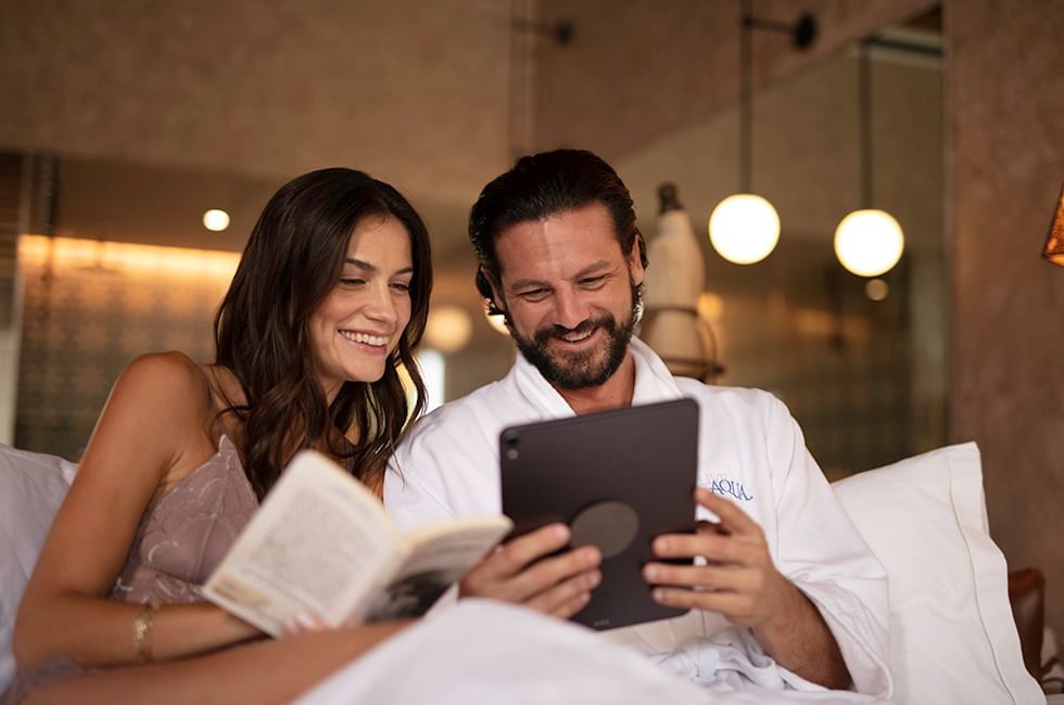 Two people reading a book and a tablet in a cozy bedroom at Live Aqua Resorts and Residence Club