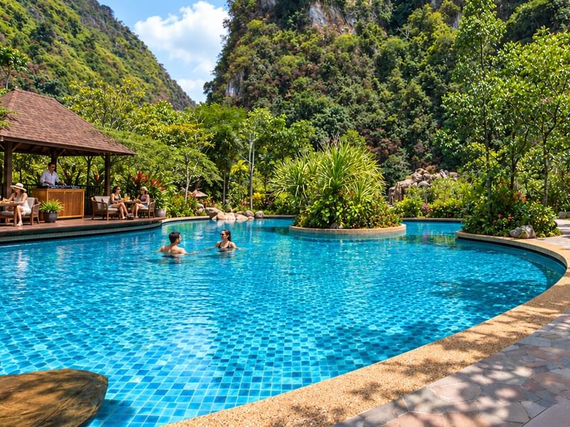 Guests enjoying pool with live DJ and barbecue surrounded by lush greenery and limestone cliffs.