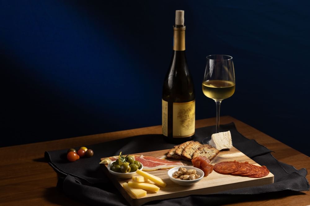 Tempting charcuterie board with cheeses, meats, olives, and bread with white wine served at El Prado Hotel