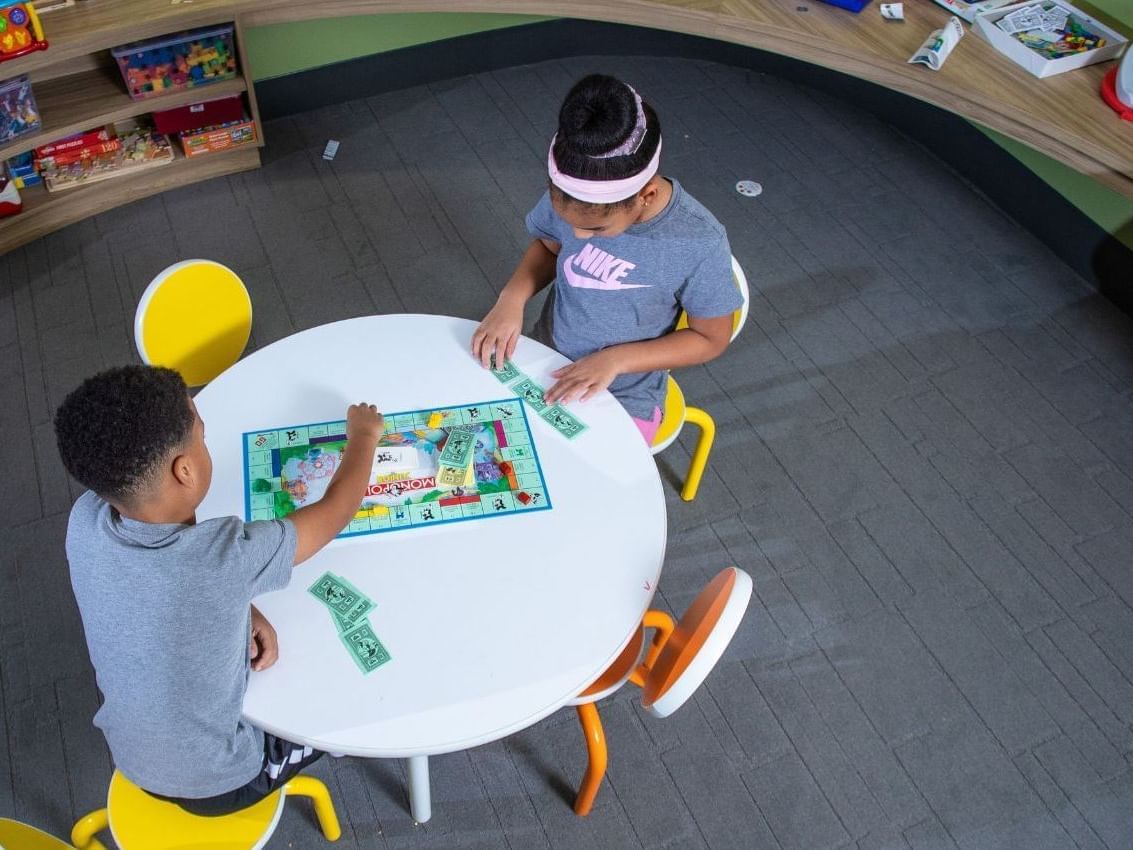 Two kids sitting at a table playing Monopoly in the Play Centre