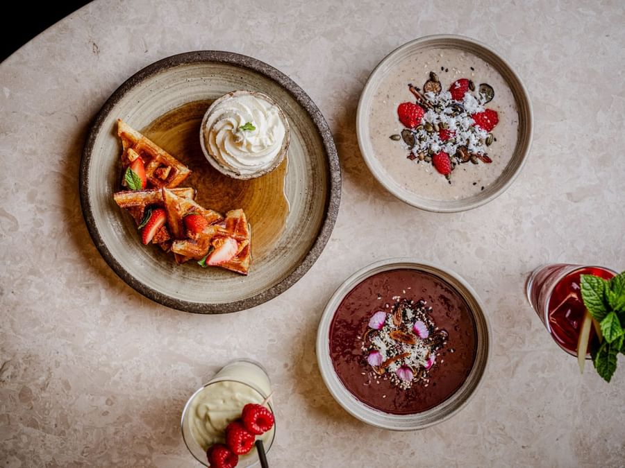 Aerial view of a brunch spread with waffles, smoothie bowls with berries, and drinks at May Fair Kitchen, The May Fair Hotel