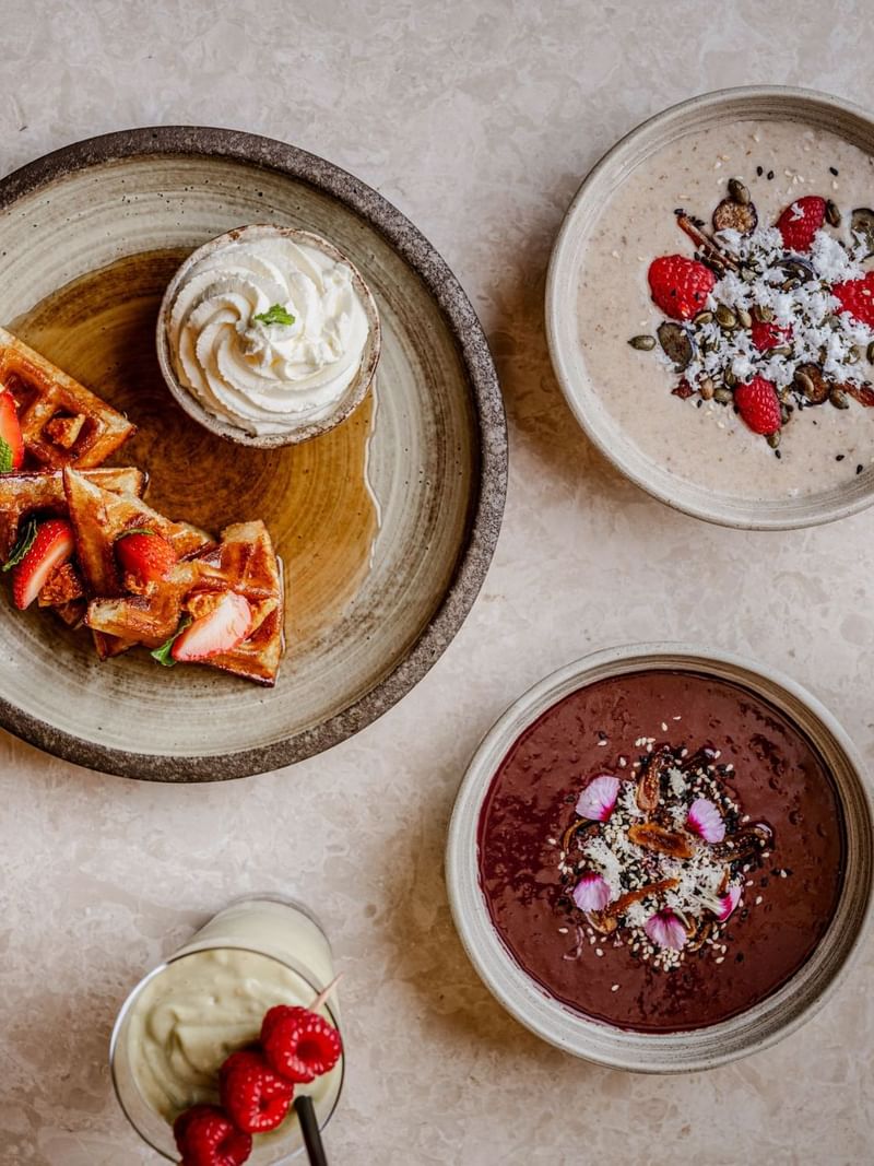 A variety of breakfast items and drinks from the By Day Menu arranged on a marble table at The May Fair Bar