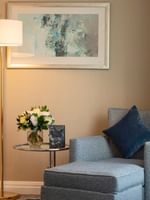 Blue ottoman and chair by a glass table under abstract wall art in The Champs-Élysées Suite at Warwick Paris Champs Elysées
