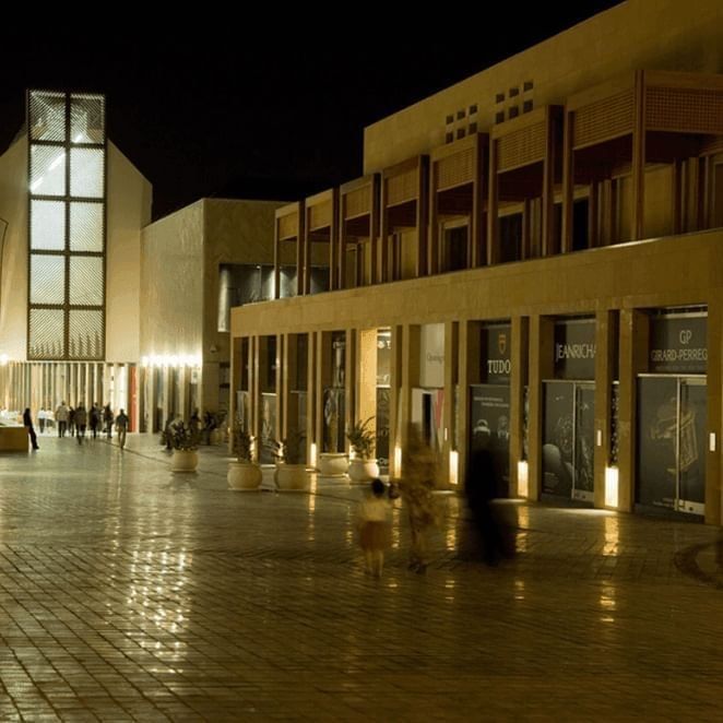 Illuminated souk walkways with potted plants by shopfronts under wooden balconies near Warwick Palm Beach Hotel