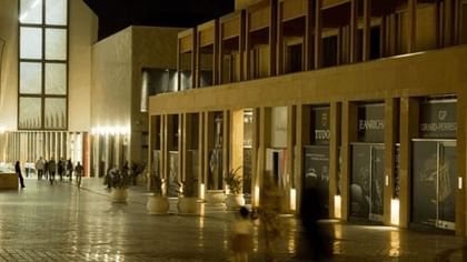 Illuminated souk walkways with potted plants by shopfronts under wooden balconies near Warwick Palm Beach Hotel