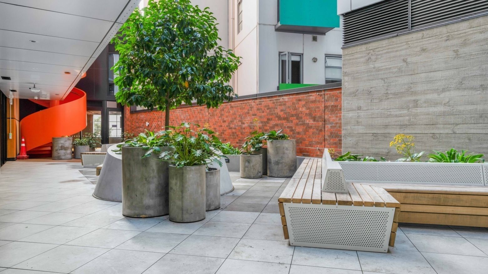 Modern outdoor courtyard with concrete planters, wooden benches, and a leafy tree at UniLodge Auckland Central