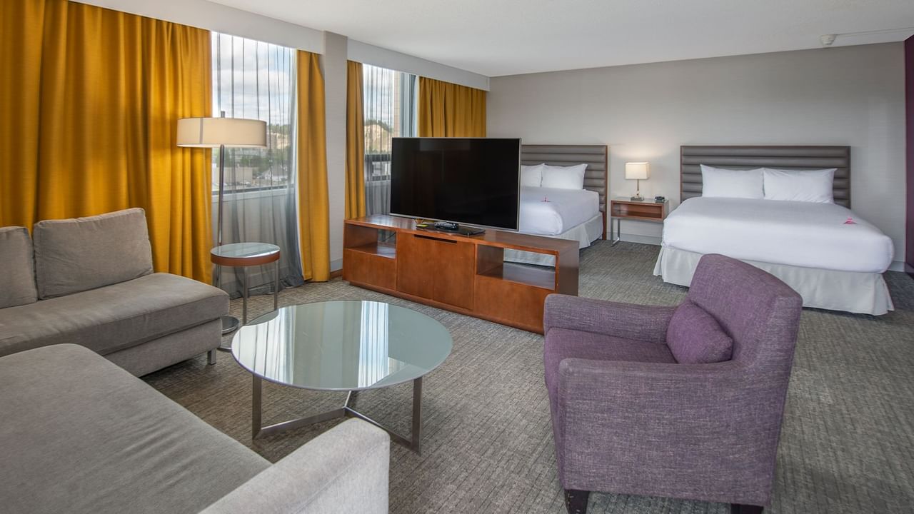 Hotel suite with two queen beds, a couch, glass table, and TV.