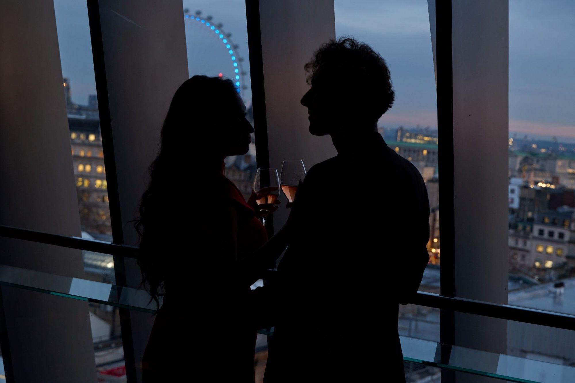 Silhouetted guests enjoying drinks by the window at dusk, overlooking the London Eye from The Londoner Hotel