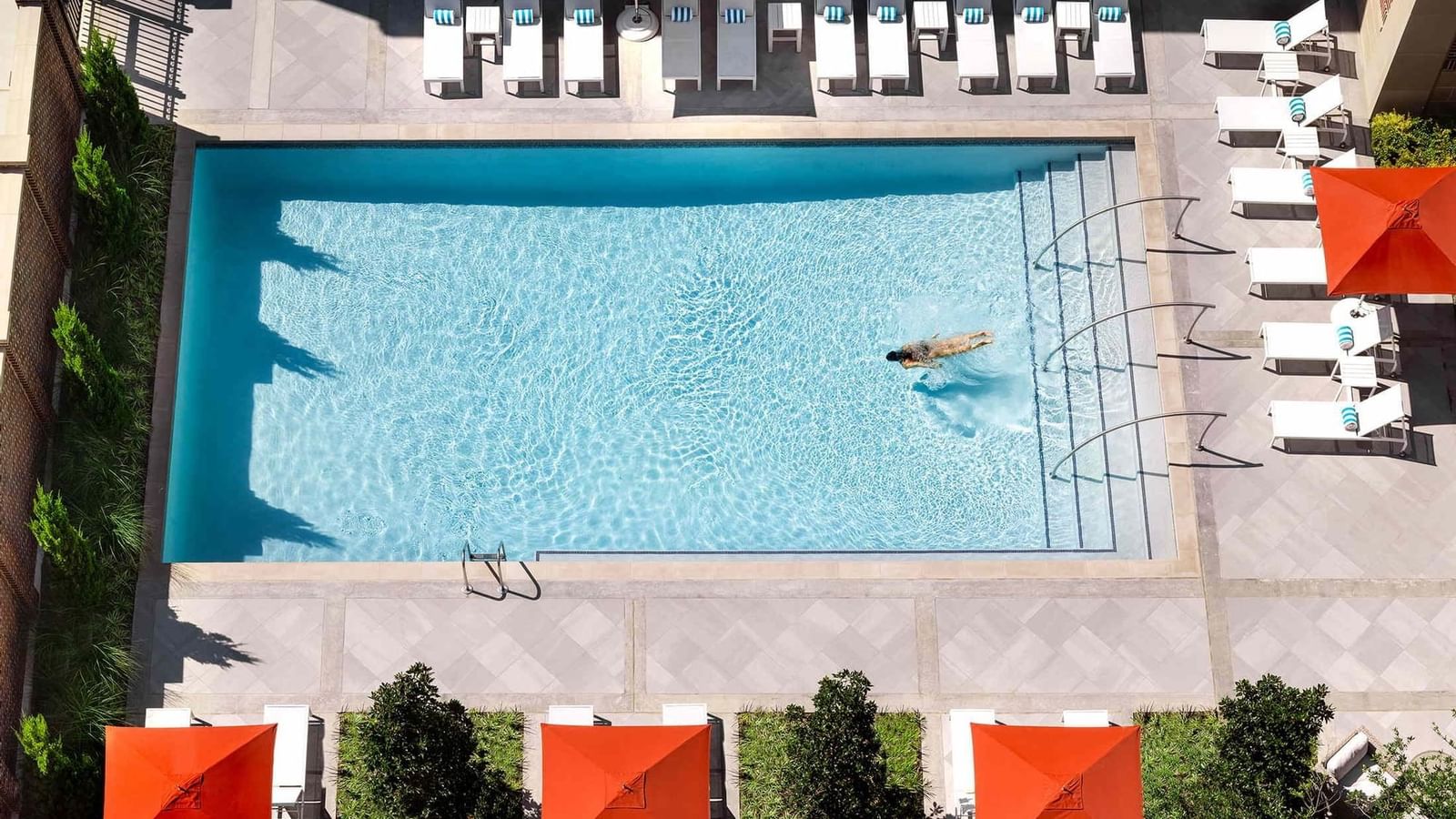 Blue pool by lounge chairs under orange umbrellas surrounding the outdoor deck at Warwick Melrose Dallas