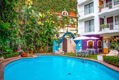 Piscina rodeada de vegetación tropical y edificios coloridos con balcones en Los Arcos Suites