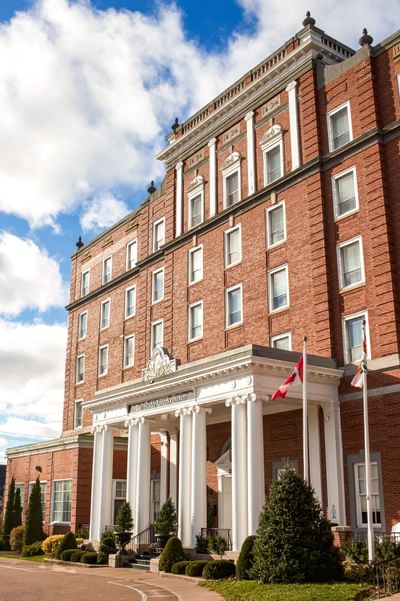 Exterior of a historic brick building with white columns by the entrance under a cloudy sky at Rodd Charlottetown Hotel