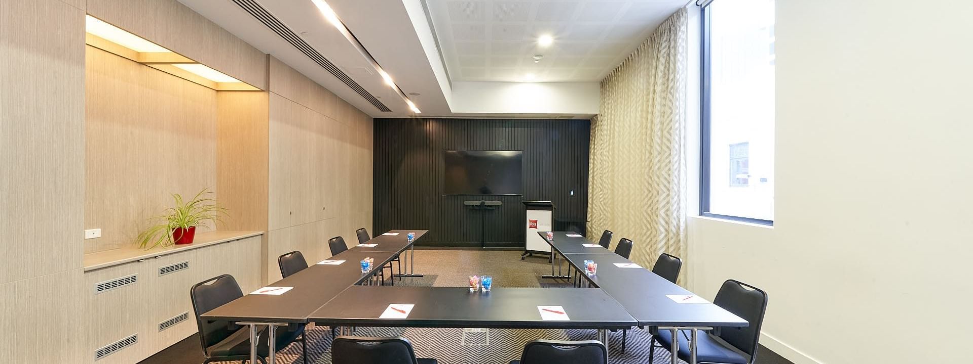 U-shape table set-up facing the wall-mounted TV in The Engine Room at Ibis Adelaide