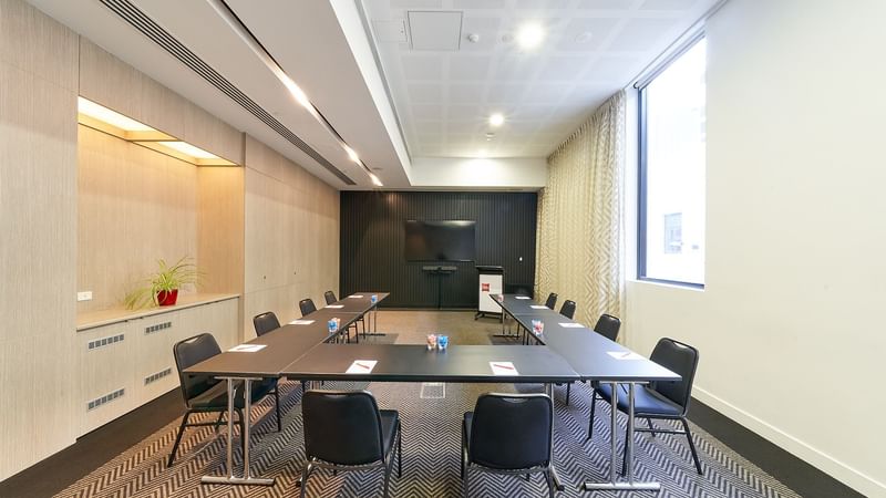 U-shape table set-up facing the wall-mounted TV in The Engine Room at Ibis Adelaide