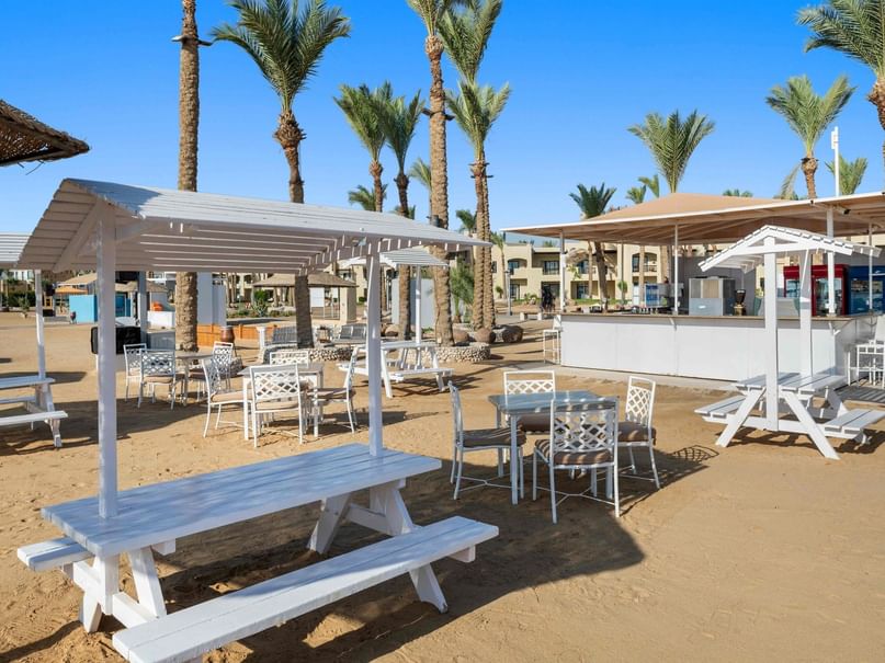 Beach Bar area with white picnic tables and chairs, shaded by canopy, at Pickalbatros Palace Hotel in Red Sea Governorate.