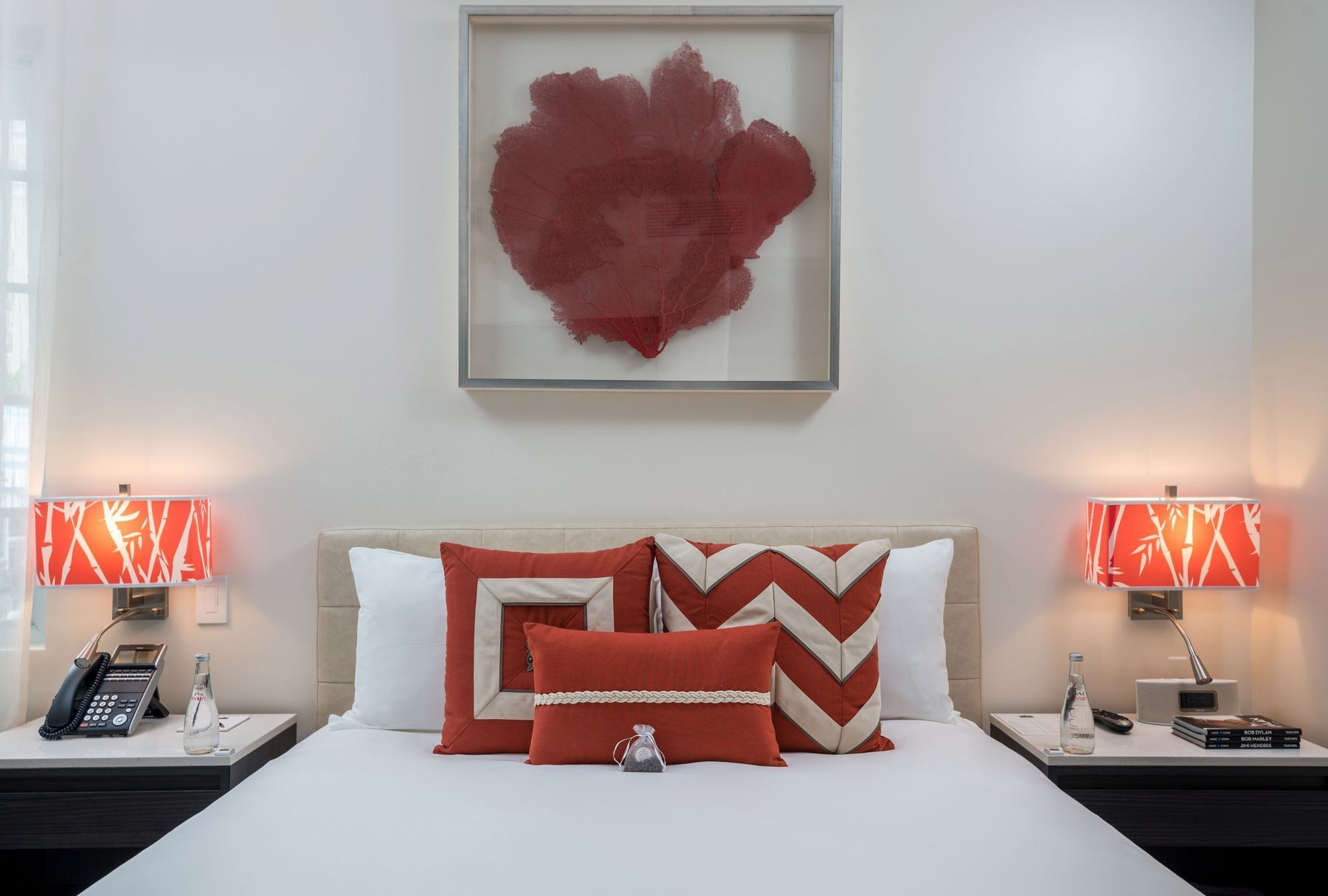 a neatly made bed with red and white pillows and a piece of artwork above it