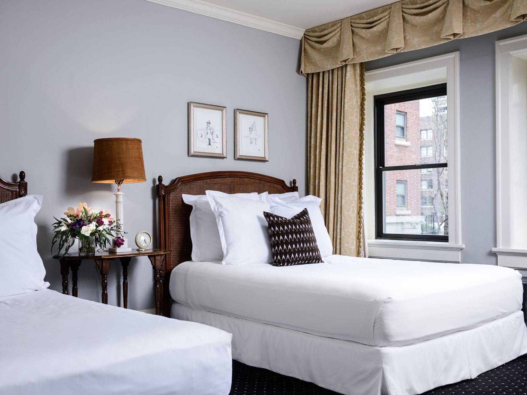 Wooden side table with a lamp and floral arrangement by the beds in Sorrento Suite 2 Queens at Hotel Sorrento