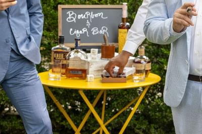 Outdoor bourbon and cigar bar setup with yellow table displaying whiskey bottles and glasses at The Ashbrook Hotel