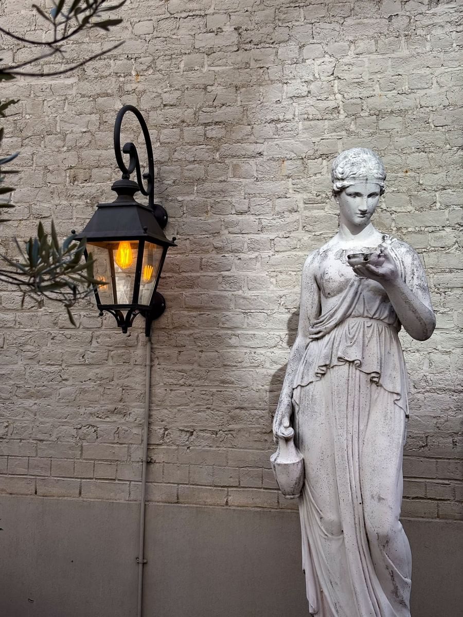 Vintage wall lantern and classical stone statue against a brick wall at Hotel Barsey by Warwick