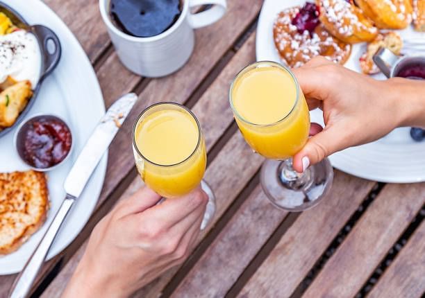 Two hands clink glasses of orange juice at a table, surrounded by a delicious brunch spread at Cove Pocono Resorts