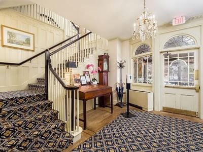Antique clock and desk with orchids by a striped staircase, under a chandelier near arched doors at Simsbury 1820 House