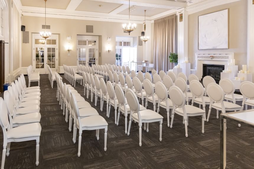 Rows of white chairs surrounding a fireplace under bright chandeliers at Rodd Charlottetown Hotel