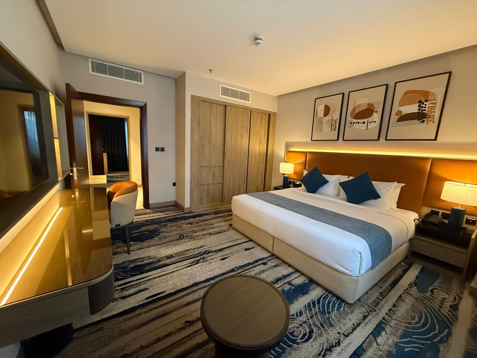 Bed with blue pillows by a wooden wardrobe and vanity desk in guest room at Warwick Jeddah Hotel & Spa
