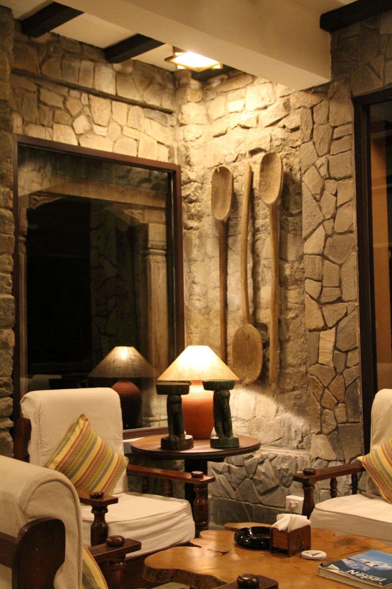 Fusion Lounge & Bar with stone walls, wooden decor, a lamp, and two chairs at Dwarika's Himalayan Wellbeing