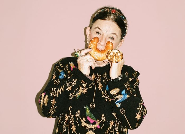 Person in a colorful black sweater holding a golden object against a pink backdrop at Hotel Motto Vienna