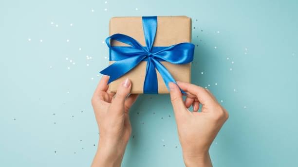 Mains tenant un cadeau emballé avec un ruban bleu sur fond bleu avec des étoiles.