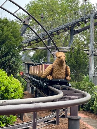 A wicker coaster car that looks like a griffin surrounded by curving metal tracks and trees. 