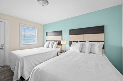 2 Double Beds bedroom featuring two beds, minimalist decor, a bedside lamp, and a window with blinds at Madison Beach Motel