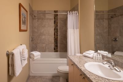 A bathroom with a bathtub, toilet, sink, and mirror, featuring towels and a framed picture on the wall.