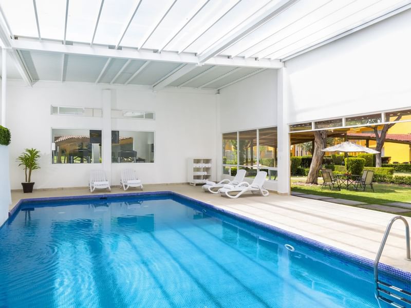 Lounge chairs by the indoor swimming pool & garden view at Hotel Gamma Pachuca