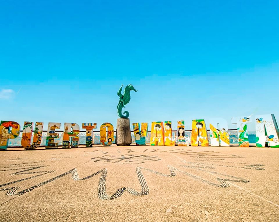 The iconic bronze seahorse statue next to the colorful Puerto Vallarta sign on a sunny beach boardwalk near Casa Dona Susana