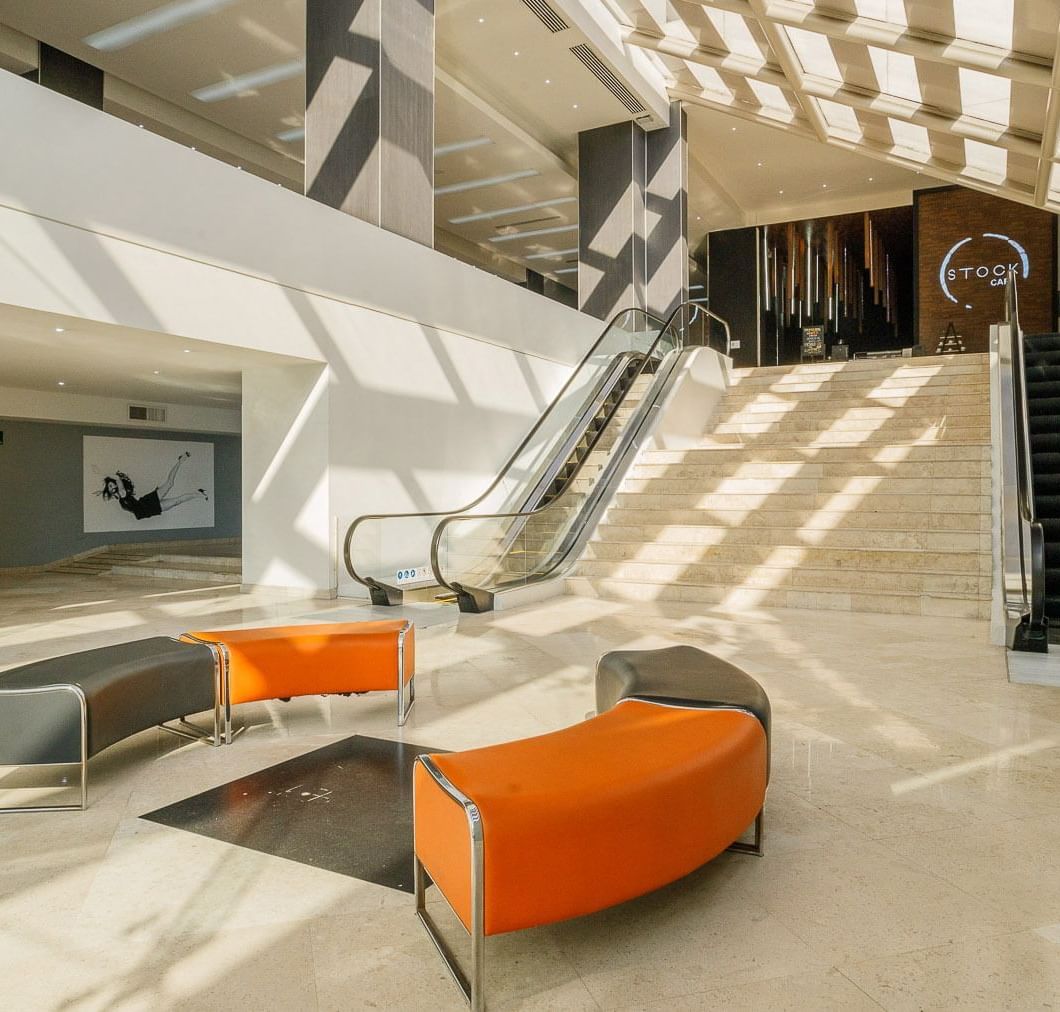 Grand lobby with orange benches by escalators, beneath a glass roof at Real Inn Tijuana