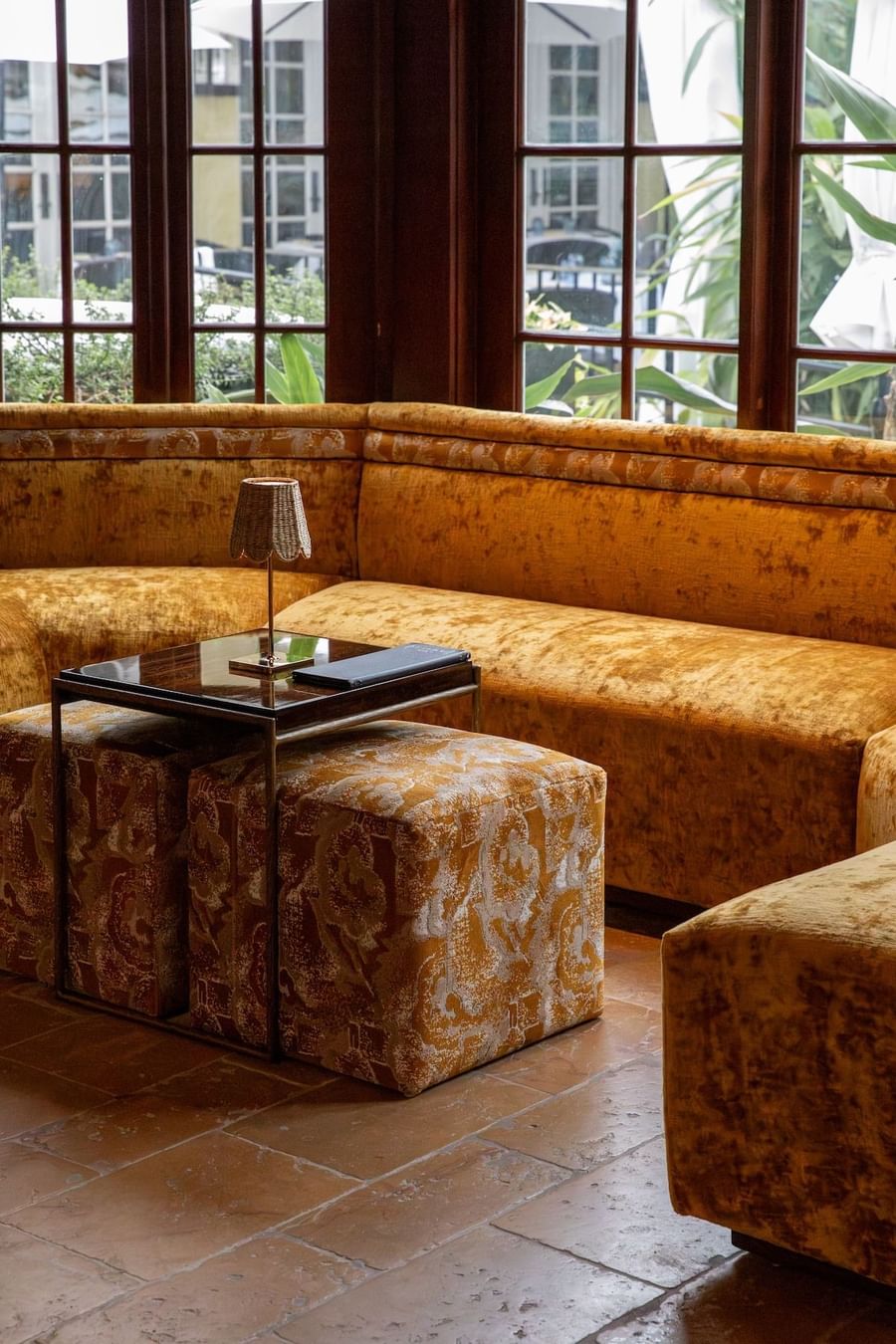 Lobby lounge yellow couch with two ottomans, table, and lamp in a room with large windows.