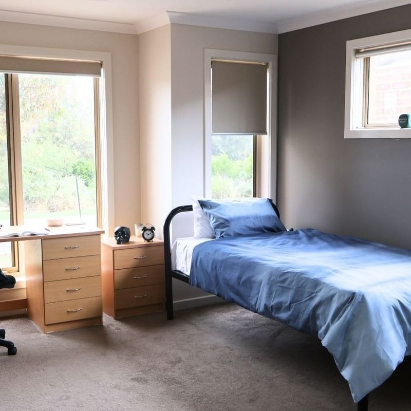 Bedroom with a single bed, desk, chair, and two windows at La Trobe University Regional Housing – Melton.