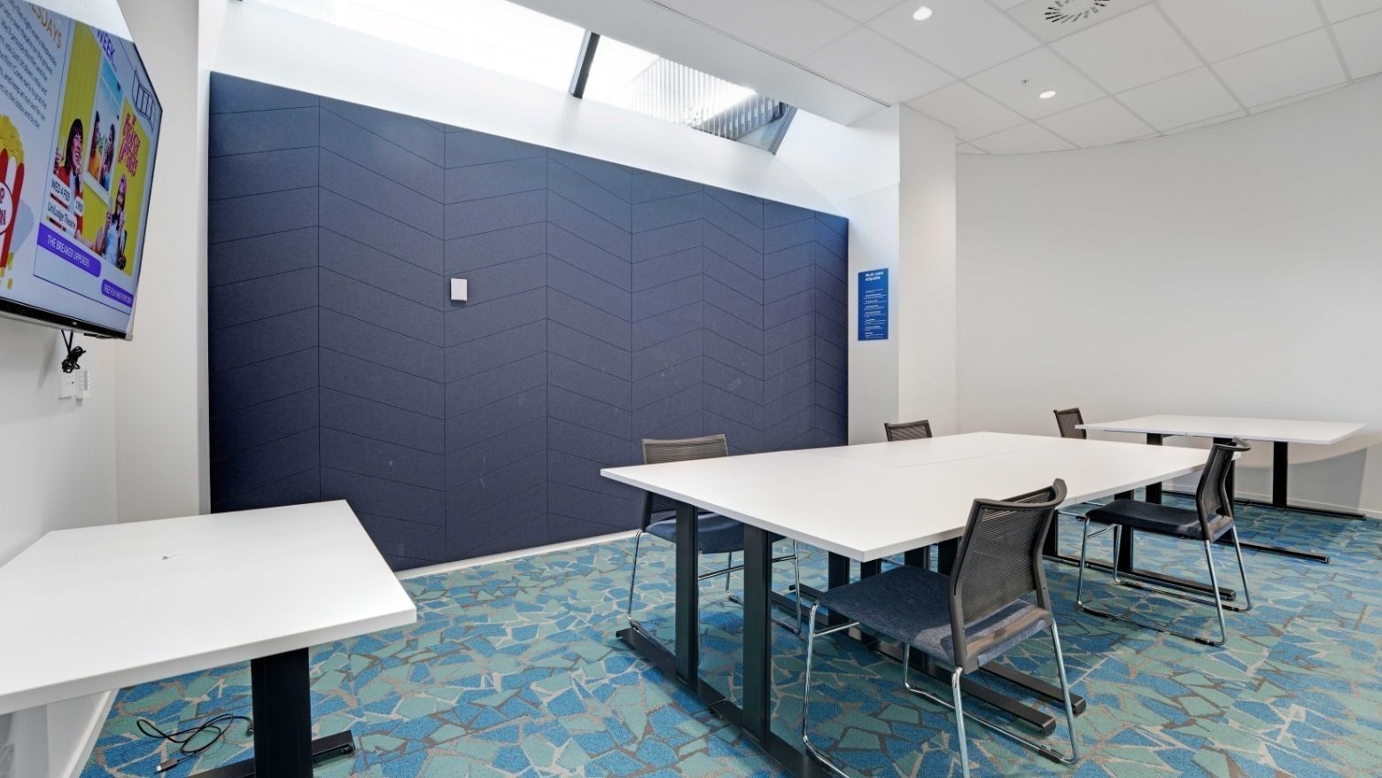 Modern study room with white tables, mesh chairs, and blue patterned carpet at UniLodge Auckland Central.