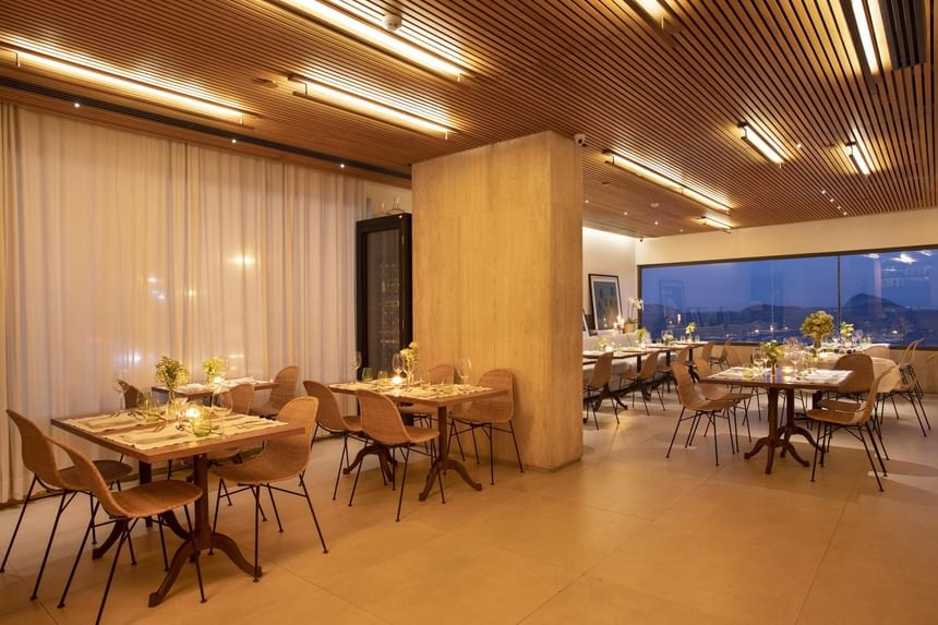 Restaurante com espaço reservado para enventos do Janeiro Hotel com mesas de jantar decoradas por flores e linda vista do leblon