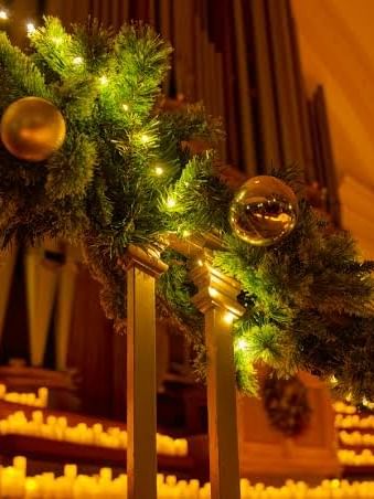 Festive garland with gold ornaments and lights beside glowing candles in a warmly lit church interior