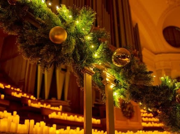 Festive garland with gold ornaments and lights beside glowing candles in a warmly lit church interior