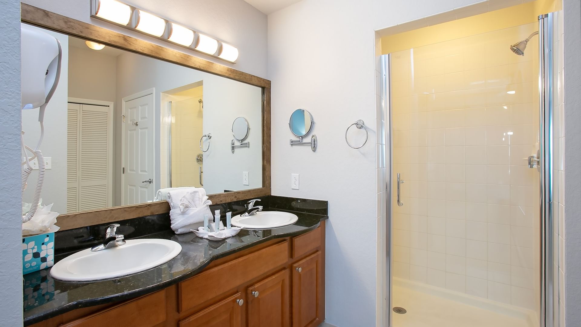 A clean bathroom with a double vanity, large mirror, and a shower in the adjacent area.